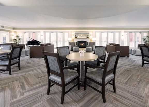 A room with a table surrounded by chairs and a piano in the background.