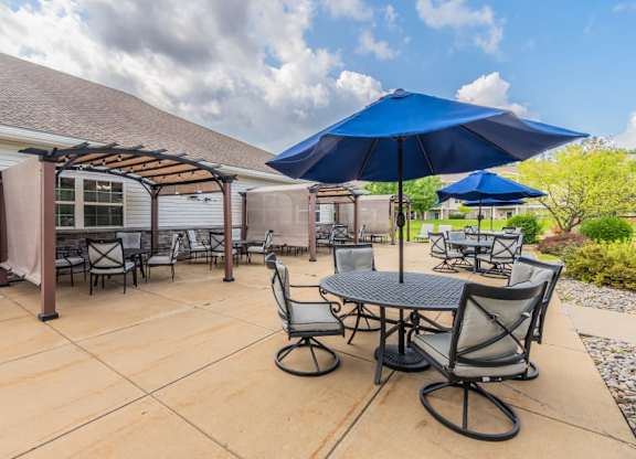 Outdoor dining patio with pergola and umbrellas at Schuyler Commons Apartments, Utica, 13502