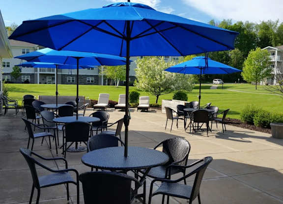 Outdoor dining area with blue umbrellas at Schuyler Commons Apartments, Utica, New York
