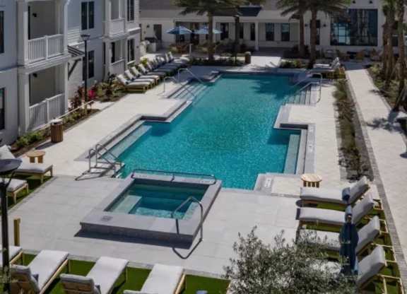 A large swimming pool surrounded by lounge chairs and palm trees. at Atwater at Nocatee Apartments, Florida
