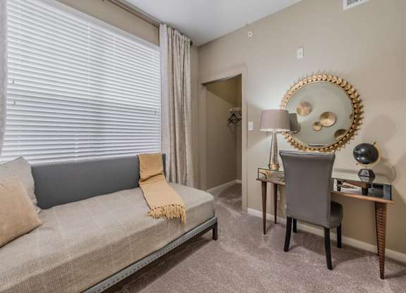 A living room with a grey couch, a chair, and a desk with a lamp. at The Spring at Silverton Apartments, Fort Worth