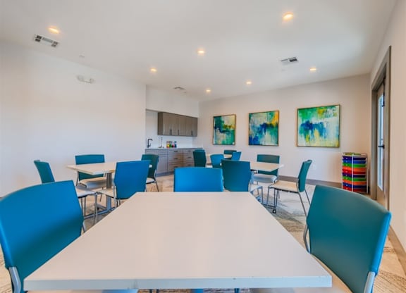 A white table surrounded by blue chairs in a room with two paintings on the wall. at The Spring at Silverton Apartments, Fort Worth, TX
