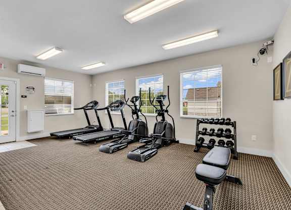 A gym with treadmills, elliptical machines, and dumbbells.