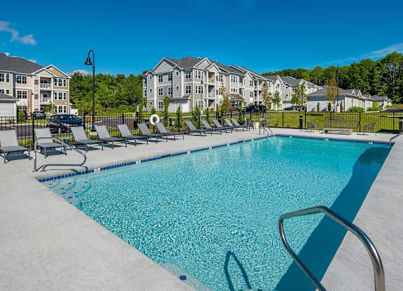 A swimming pool surrounded by lounge chairs and apartment buildings in the background.