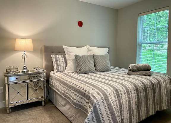 A bedroom with a bed, nightstand, and window.