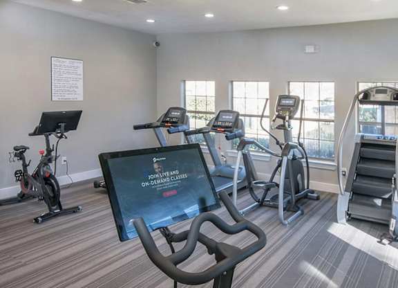 A gym with treadmills, exercise bikes, and a television screen showing a fitness program.