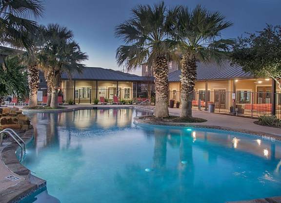 A pool surrounded by palm trees at night.