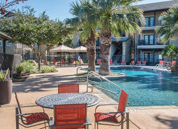 A poolside table with chairs is surrounded by palm trees.