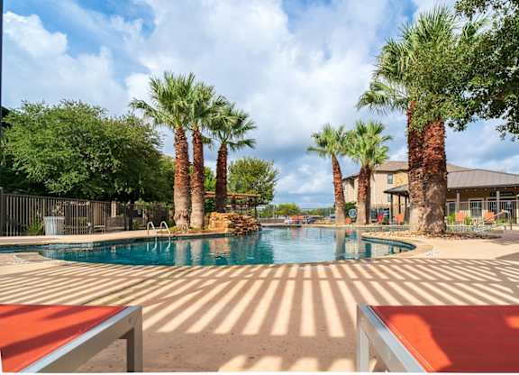 A pool surrounded by palm trees and a red bench.