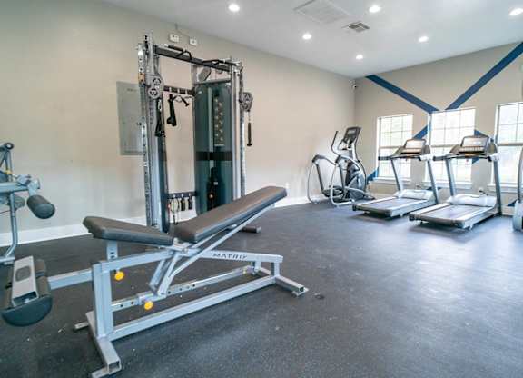 A gym with a variety of equipment including treadmills, a leg press machine, and a bench press.
