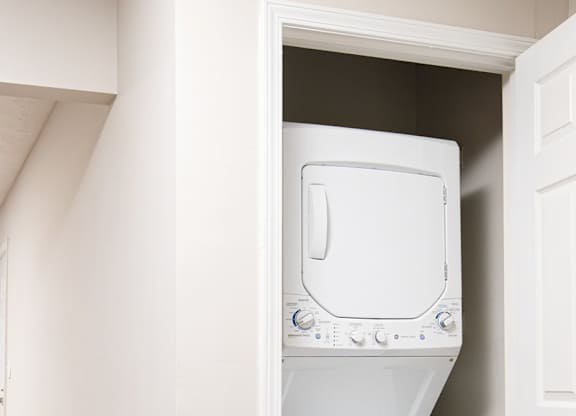 A white washing machine is in a small space between a wall and a door.