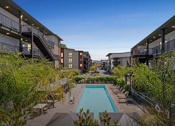 A pool surrounded by lounge chairs and trees in a courtyard.