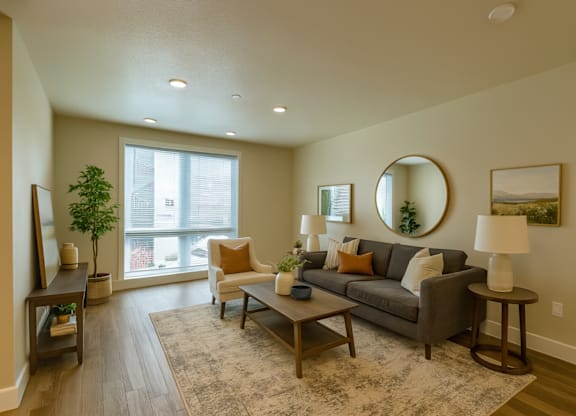 A living room with a grey couch, a coffee table, a side table, a lamp, a mirror, and a potted plant.