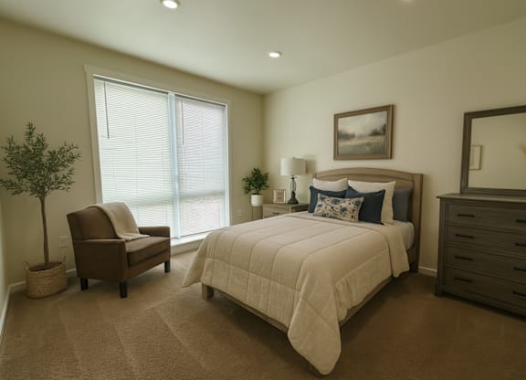 A well-lit bedroom with a large bed, a chair, and a potted plant.