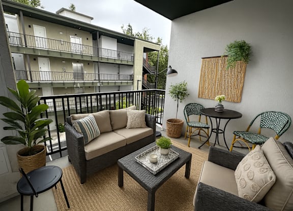 A balcony with a couch, chairs, and a table with a potted plant on it.