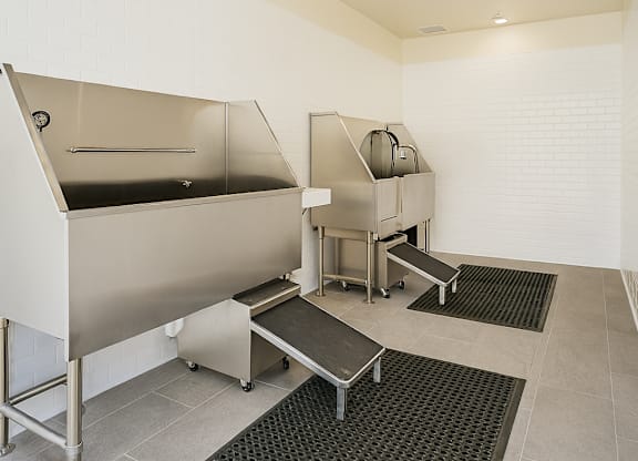 A clean, empty industrial kitchen with stainless steel appliances and black mats on the floor.