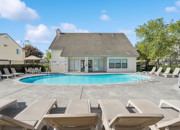 A house with a pool and lounge chairs in front.