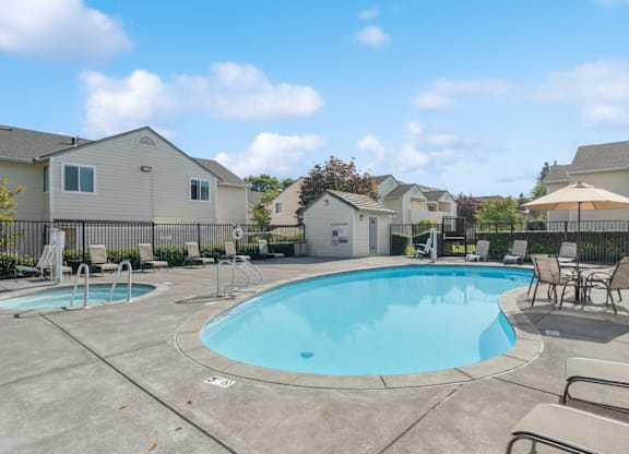 A swimming pool surrounded by lounge chairs and umbrellas in a residential area.