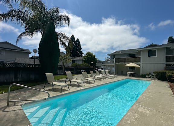 A swimming pool surrounded by chairs and trees.