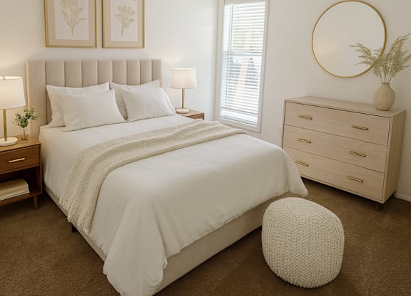 A white bedroom with a large bed, a round mirror, and two framed pictures on the wall.