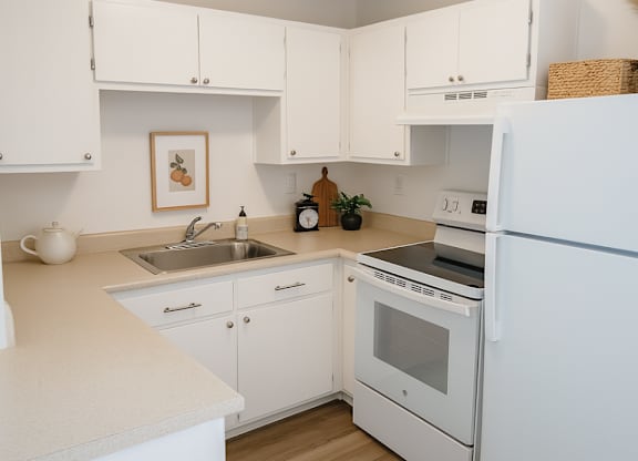 A white kitchen with a fridge, oven, and sink.