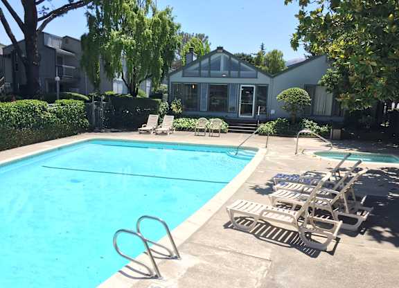 A pool with chairs and a building in the background.