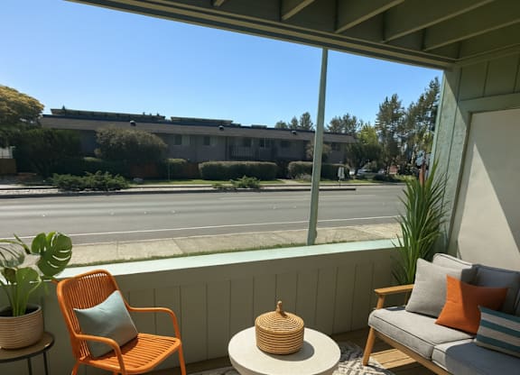 A patio with a chair, a table, and a couch with a view of the street.