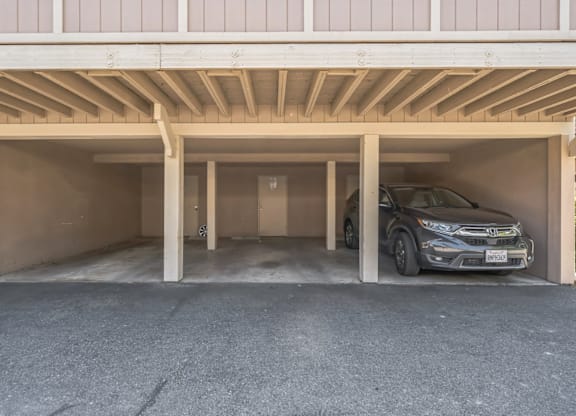 A car is parked in a garage under a wooden beam.