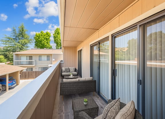 A balcony with a couch and a table with a glass door.