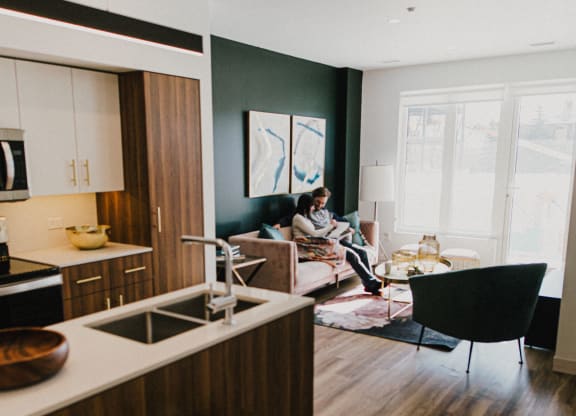 a living room and kitchen with a woman sitting on a couch