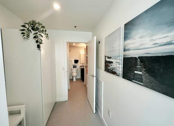 A hallway with a painting on the wall and a plant on the side.