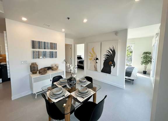 A dining room with a table set for two and a painting of a bird on the wall.