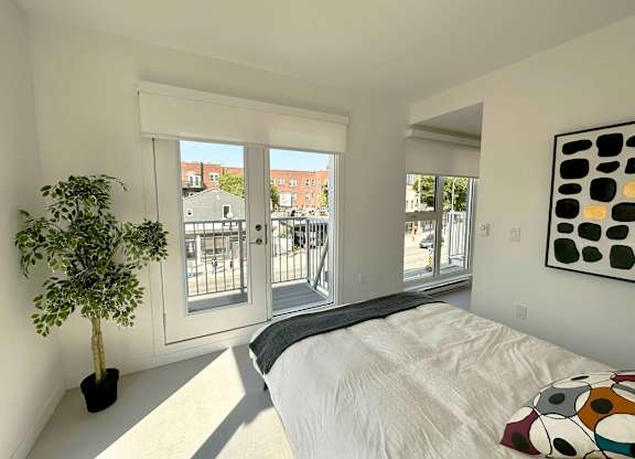 A bedroom with a bed, a potted plant, and a painting on the wall.