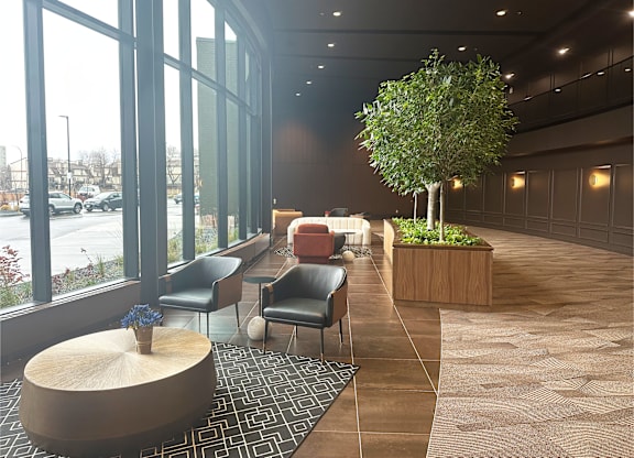 A tree in a planter stands in a hallway with a couch and chairs.