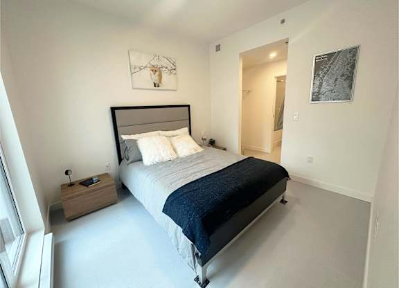 A bedroom with a bed, nightstand, and artwork on the wall.
