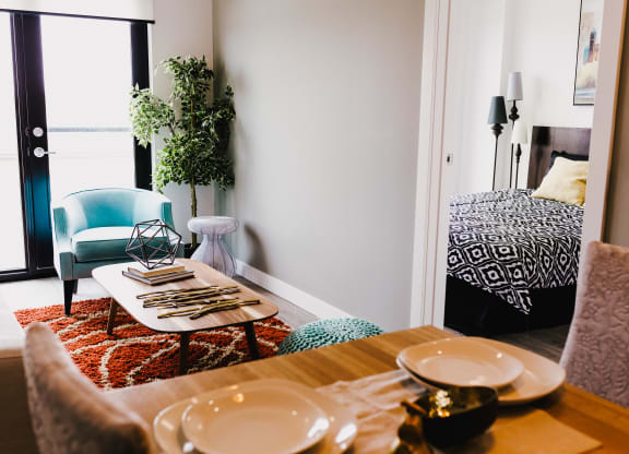 a living room with a dining table and a bed in the background