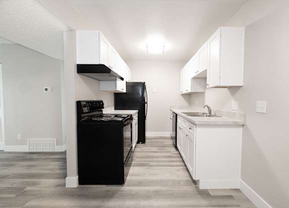 A black refrigerator sits in a kitchen with white cabinets.