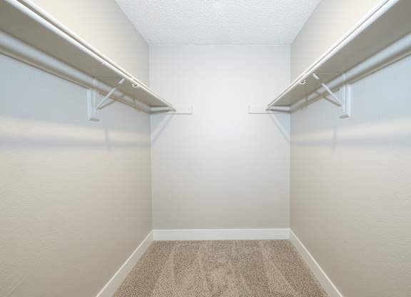 A white closet with two shelves and carpeted floor.