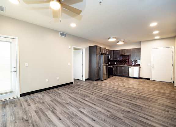 the living room and kitchen of a new home with wood floors and a ceiling fan