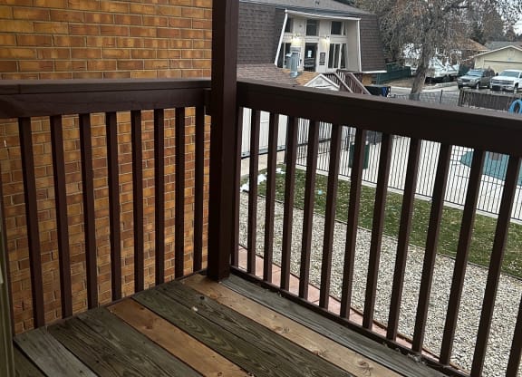 a deck with a wooden railing and a house in the background