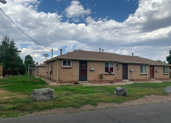 a brown brick house with a grass yard and rocks