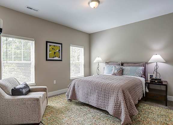 A bedroom with a bed, chair, and lamp.