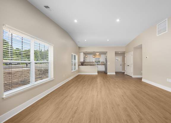 A large empty room with wooden floors and a window with blinds.
