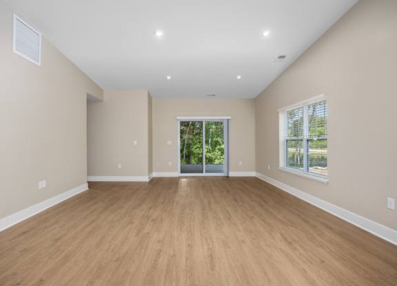 A spacious room with wooden flooring and a sliding glass door leading to a balcony.
