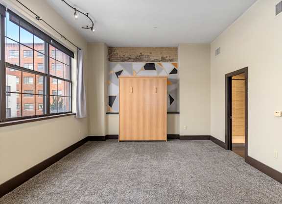 A room with a wooden wardrobe and a window overlooking a building.