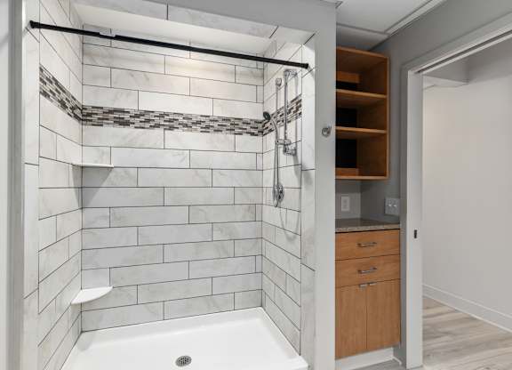 A bathroom with a white tiled shower and a wooden cabinet.