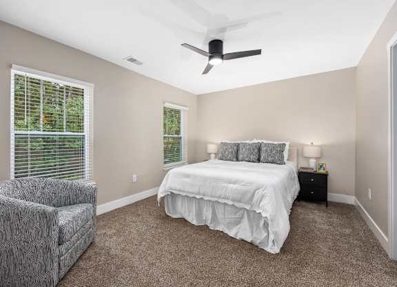 A bedroom with a bed, chair, and ceiling fan.