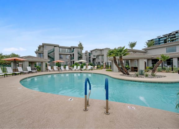 A swimming pool surrounded by lounge chairs and palm trees.