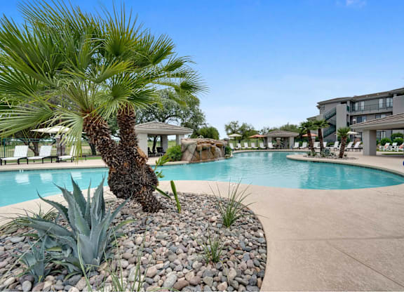 A palm tree stands in a rock bed next to a pool.