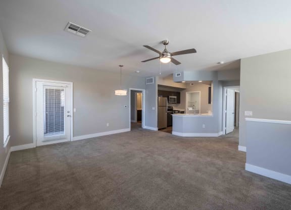 an empty living room with a ceiling fan and a kitchen